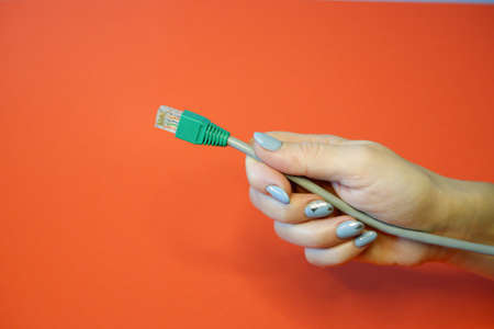 Green RJ45 network connector on a red background in well-groomed female handsの写真素材