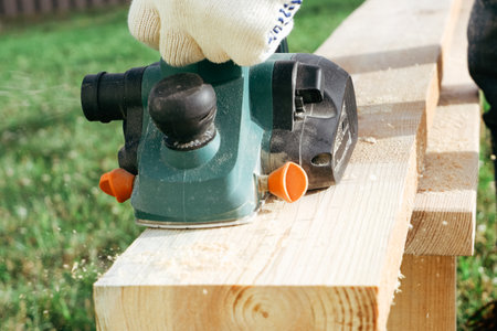 A builder is planing a board at the construction of a new house. Close-up on gloved hands with an...