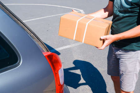 Young male shopper stacks cardboard boxes in the trunk of a car in a supermarket parking.