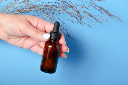 Beautiful groomed woman's hands with serum bottle on blue background. Pattern of beauty products packagingの写真素材