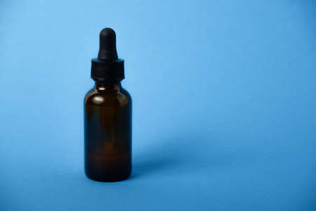Essential serum oil in amber dropper bottle. Serum glass bottle with pipette on blue background.の写真素材
