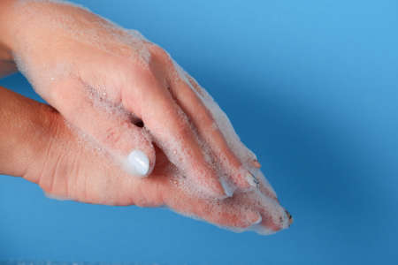 Bubble bath foam in woman's hands. Closeup woman's hand washing with soap on a blue background, selective focus. Hygiene and health protectionの写真素材