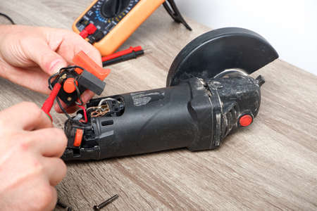 Power tool repair. A man repairs an angle grinder. Screwdriver, multimeter.
