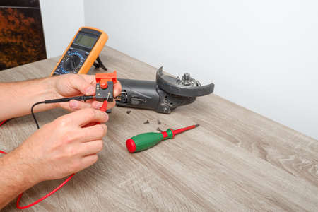 Power tool repair. A man repairs an angle grinder. Screwdriver, multimeter.