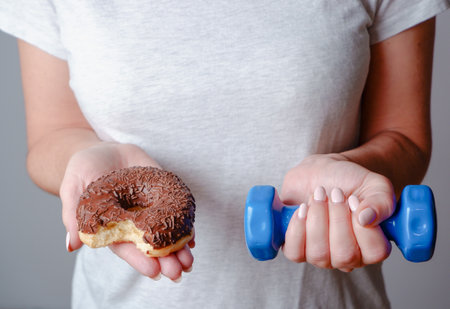 Diet. Woman Holding Donut and Dumbbell. Sweets Are Unhealthy Junk Food.の写真素材
