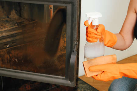 Cleaning the fireplace. Women's hands in orange rubber gloves wash the heat-resistant glass of the...