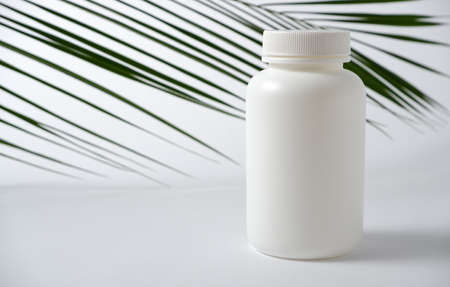 White plastic bottle for vitamins, cosmetics, health care products on a white background with green palm leaves.の写真素材