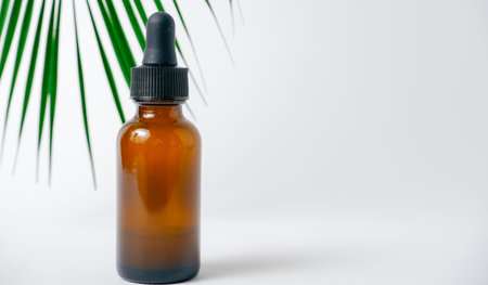 Essential oils on white background with palm leaves, mockup. Cosmetic medical beauty product in brown glass bottles with a pipetteの写真素材