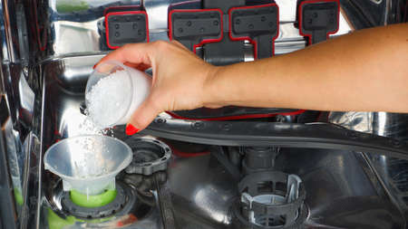 Adding salt to the dishwasher. A woman's hand pours salt to soften the water into the dishwasher.の写真素材