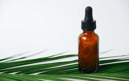 Essential oils on white background with palm leaves, mockup. Cosmetic medical beauty product in brown glass bottles with a pipetteの写真素材