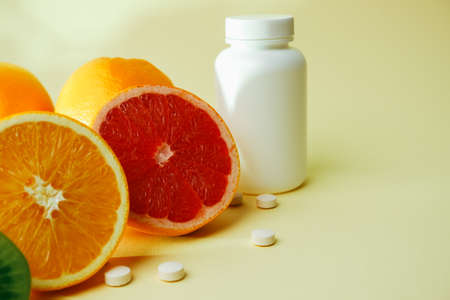 Vitamins. Medical concept. Pharmacy or natural. White bottle with vitamins, scattered pills. Juicy citrus fruit slices. lemon. Orange. Grapefruit.の写真素材