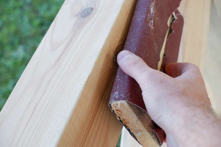 Sanding wood. A male carpenter is sanding the wooden beams of a made gazebo. Hand of a Carpenter Rubbing Wood With Sand Paperの写真素材