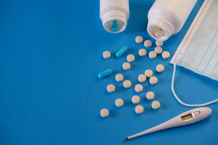 medicine and health concept. Pills, thermometer and medical mask on a blue background. Place for...