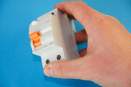 A man's hand holds a white, automatic differential current switch. electrical engineering concept.の写真素材