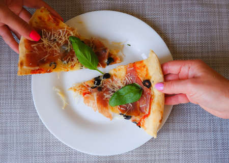 Close-up top view of a female hand takes a slice of pizza from a white plate. Appetizing delicious...