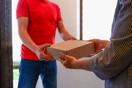 A delivery courier hands over cardboard boxes of goods to a woman near the door of her house.の写真素材