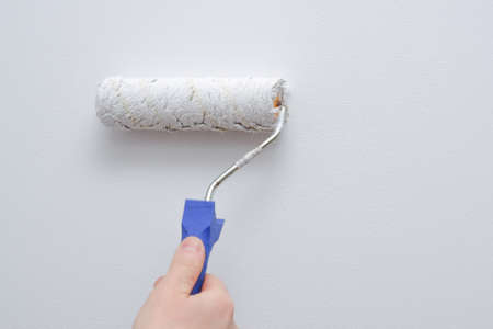 painting works. A man paints a light wall with a paint roller. Close-up on a hand with a tool.の写真素材