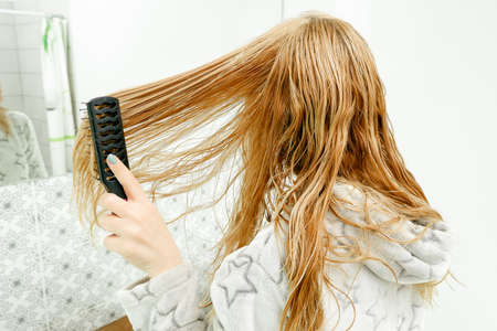 A blonde woman tries to combine her tangled hair with a comb after bathing. Red blond combing wet...
