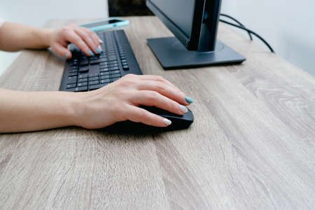 Businesswoman working on a computer from home during pandemic to prevent disease. remote work. Hands, mouse, keyboard. Cropped shot of woman typing on keyboard and working with desktop computerの写真素材