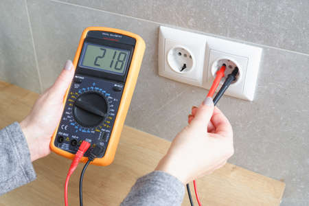 Woman with a multimeter check the voltage of the electrical network. Close-up view of the hands with...