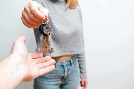 Focus on female hand holding house keys. Woman realtor giving a bunch to new happy owner of...