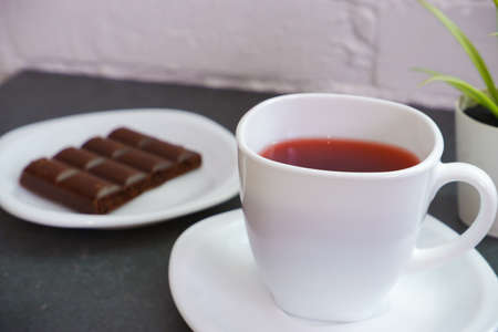 Sweet chocolate snack. White cup of tea close-up of a bar of chocolate in the background. World Chocolate Day snack or breakfast concept.の写真素材
