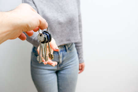 Focus on female hand holding house keys. Woman realtor giving a bunch to new happy owner of...