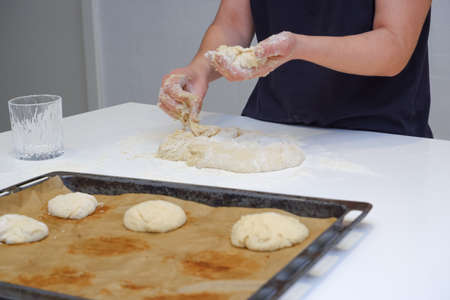 DIY home cooking concept. A young woman works with yeast dough in a modern kitchen. A young woman is kneading a dough, engaged in cooking homemade bakery.の写真素材