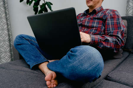 Male freelancer working working on a laptop from home, sitting cross-legged on the couch. Caucasian...