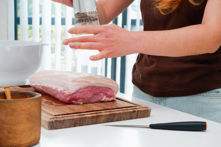 A young woman prepares meat on a white surface in a modern bright kitchen. Modern minimalistic bright kitchen, close-up photo. woman preparing food in the kitchenの写真素材