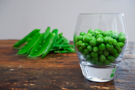 Green peas in glass bowl. fresh pea in the pod with green leaves. green peas on a brown wodden table. Shelled peas in a glass with the pods on the sideの写真素材