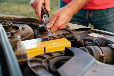 The Mechanic hand is pulling up an old car battery for replacement. A man tightens with a wrench...