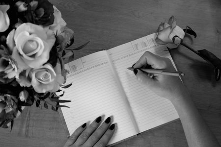 Female hands writing in open notebook and bouquet of roses on old wooden table. Planning notebook...