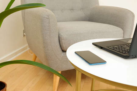 Remote work from home. Laptop on a white coffee table near the armchair. The workplace of...