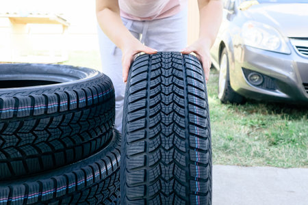 Woman putting hand on new wheel tire. Female holding a tire and standing next to a pile of tires....
