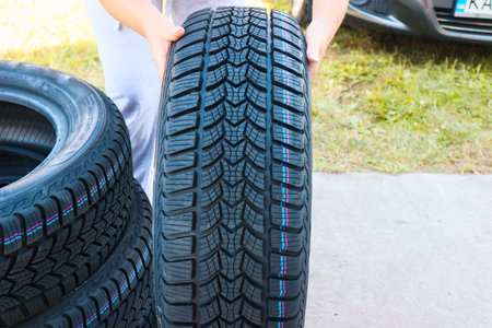 Woman putting hand on new wheel tire. Female holding a tire and standing next to a pile of tires. Auto car repair serviceの写真素材