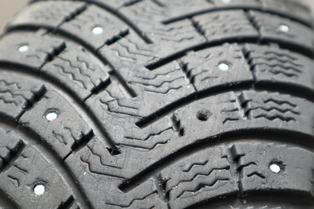 Winter car tire repair. Worn tire tread, winter studded tire - wheel repair service. Renew Lost studs. Old winter studded tire close up. Used snow tire with missing steal studs closeup.の写真素材