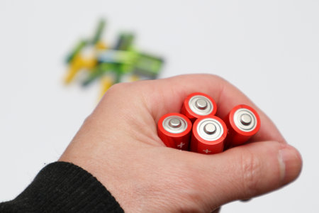 Close up of positive battery ends, selective focus. Used battery for recycling. Hazardous garbage concept. Red colors of batteries in hand on a white backgroundの写真素材
