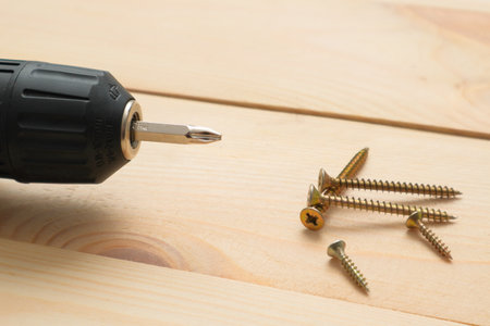 Table with tool. Electric screwdriver on a wooden table. Side view of the black metallic screws, electric screwdriver on the wodden boards.の写真素材