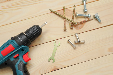 set of tools on wooden table, a electric screwdriver with a set of drill bits and screws with bolts....