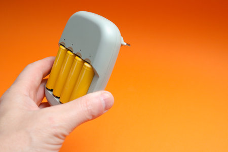 Charger and Batteries in male hand. Male hand holding charger with yellow AA batteries, on on orange backgroundの写真素材