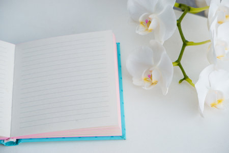Paper note pad on white table with magnolia flowers. Holiday photography concept. Flower with open notebook on white tableの写真素材