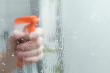 Hand holding glass cleanser spray. Hand spray detergent on the mirror. spraying liquid to the glass.の写真素材