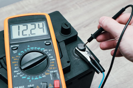 Check and charge car battery with charger. Person measures voltage. Selective focus an auto mechanic uses a multimeter voltmeter to check the voltage level in a car battery.の写真素材