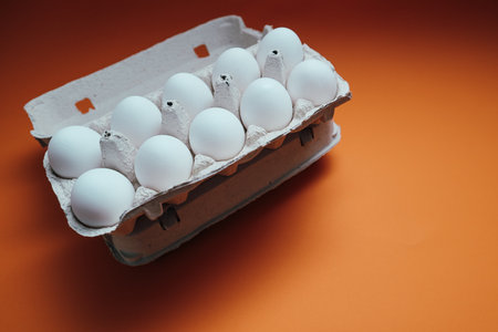 Ten white eggs in a cardboard package. Cardboard egg box on orange background. Dozen eggs in open...
