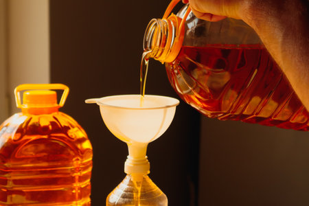A man Pouring golden sunflower oil from a large plastic bottle.