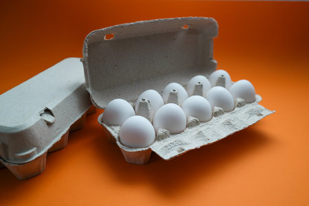 Ten white eggs in a cardboard package. Cardboard egg box on orange background. Dozen eggs in open...