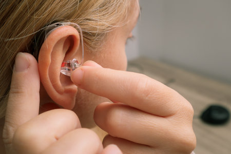 Close up of Woman inserting her hearing aid into ear. Blonde Woman with Modern Hearing Aid. Hearing...