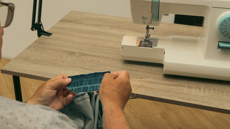 Elderly male tailor sews on a sewing machine. Tailor sewing cloth with sewing machine at sewing workshopの写真素材