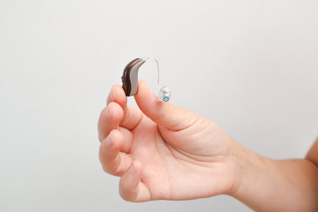 Happy woman holding last generation of hearing aid in hand. The girl is watching types of hearing...